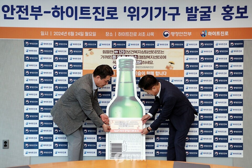 24일 오전 서울시 서초구 하이트진로 서초동사옥에서 열린 '행정안전부-하이트진로 위기가구 발굴 홍보 협약식'에 참석한 장인섭 하이트진로 전무(오른쪽)와 구본근 행정안전부 스마트복지안전공동체추진단장(왼쪽)이 홍보라벨을 부착하고 있다. / 사진제공=하이트진로