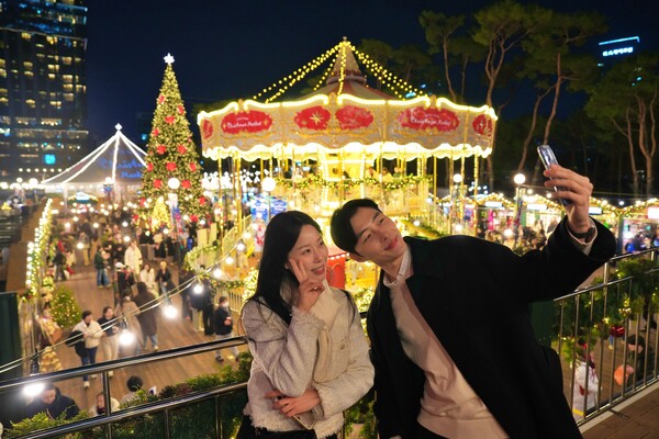 롯데타운 잠실 크리스마스 마켓에서 2층 회전목마와 초대형 크리스마스 트리 를 배경으로 사진을 찍는 모델 / 사진=롯데쇼핑
